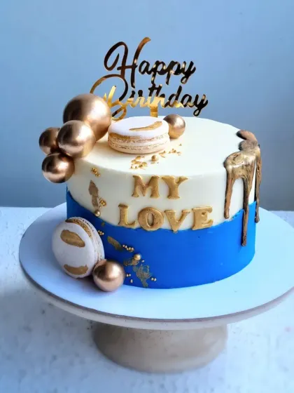 A stylish birthday cake for a loved one, in blue and gold. This design features a gold drip, macarons, and chocolate spheres.