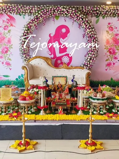 A baby shower setup with a beautiful floral ring backdrop and a modern chaise lounge. The plate decoration is traditional and colorful.