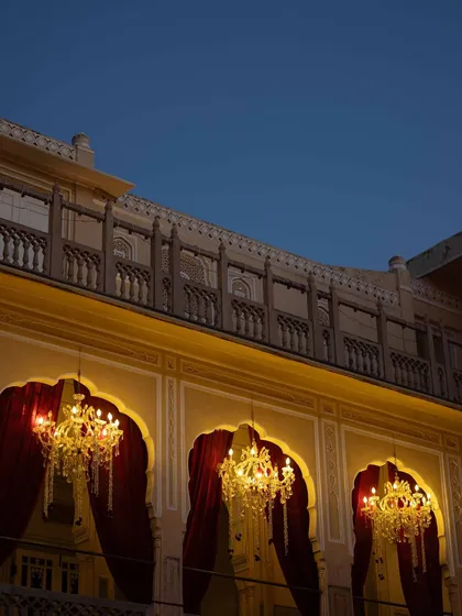 The palace walls at dusk, with grand chandeliers illuminating the arched windows. We use lighting to transition the venue from day to night seamlessly.