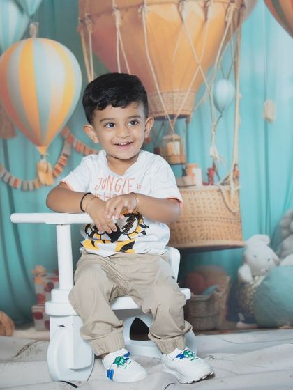 A smiling toddler sits happily on a white toy tricycle during his fun studio photoshoot.