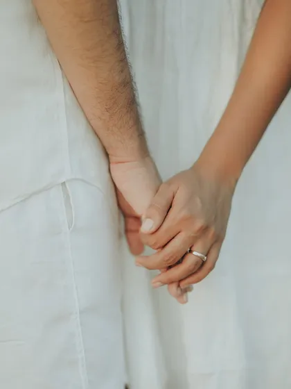 A simple, powerful shot of a couple holding hands. This close-up focuses on their intertwined fingers and the wedding ring, symbolizing their bond.