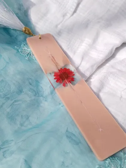 This bookmark features a single, vibrant red flower embedded in the center of a nude-pink resin base. It's a simple, elegant design for any book lover.