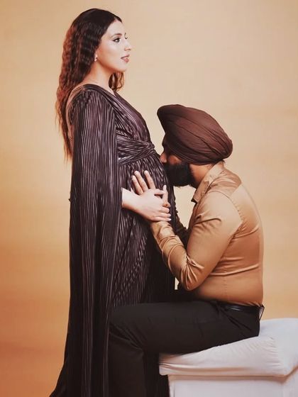 A classic pose celebrating the baby bump. The father-to-be kisses his partner's belly, a beautiful gesture of love and anticipation. The dark gown provides a classic and sophisticated silhouette.
