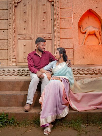 A couple sits on the steps in front of a rustic, carved doorway, creating a relaxed and intimate scene.