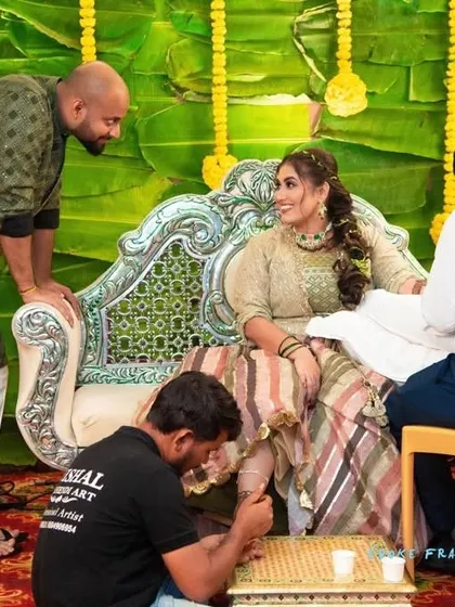 A candid moment from a mehandi ceremony, with the bride and groom admiring the artwork.