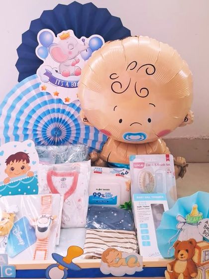 This welcome hamper for a baby boy features a large baby-faced balloon and an adorable elephant motif. It's filled with practical items like baby wipes, clothes, and a pacifier.