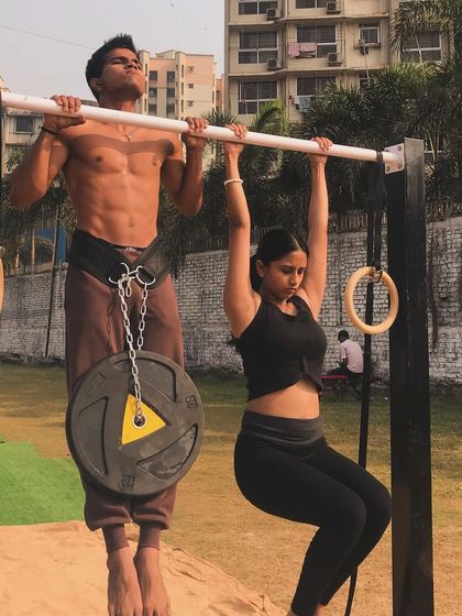 A demonstration of a weighted pull-up next to a hanging hold. This shows different levels of progression within the same exercise.