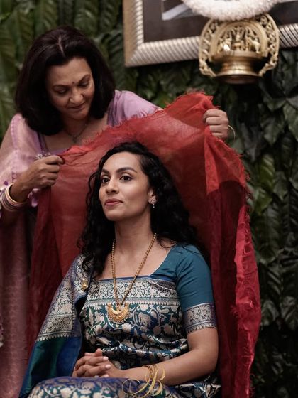 A beautiful moment as a mother drapes a red veil over her daughter, with the rich green coffee leaf wall providing a stunning, textured background.