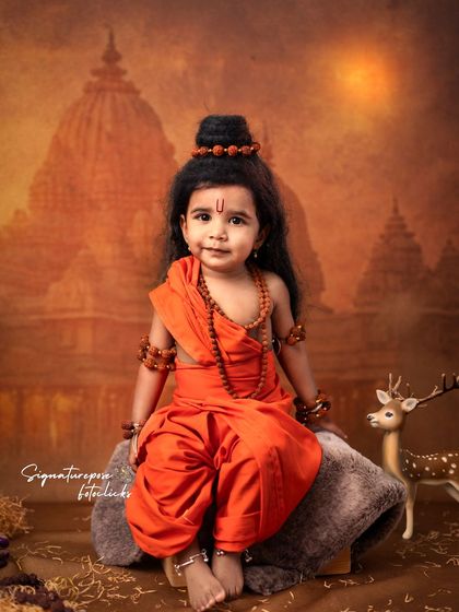 A charming portrait of a little girl dressed as Lord Rama, sitting gracefully against a temple backdrop.