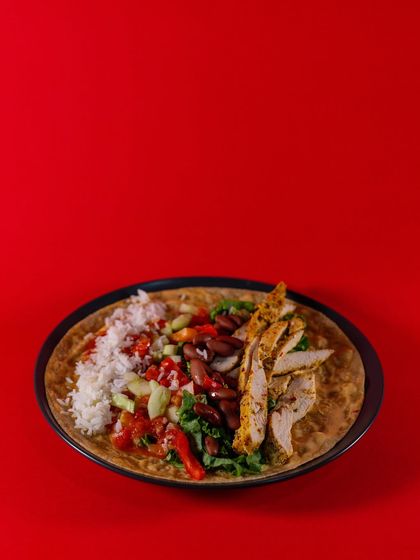 Our Chicken Burrito Wrap is a complete meal. This image shows the deconstructed wrap with seasoned grilled chicken, rice, kidney beans, and fresh salsa on a whole wheat tortilla.