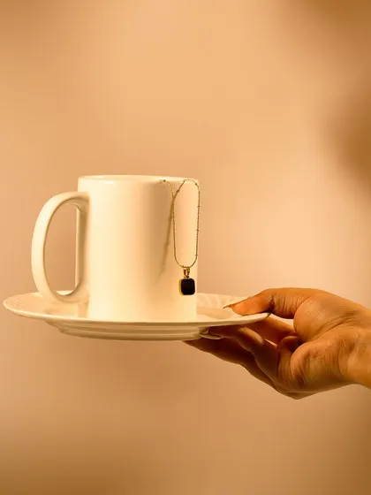 A hand serving a coffee cup with a necklace draped over it. This is another creative and unconventional way to showcase jewelry, blending everyday objects with luxury.