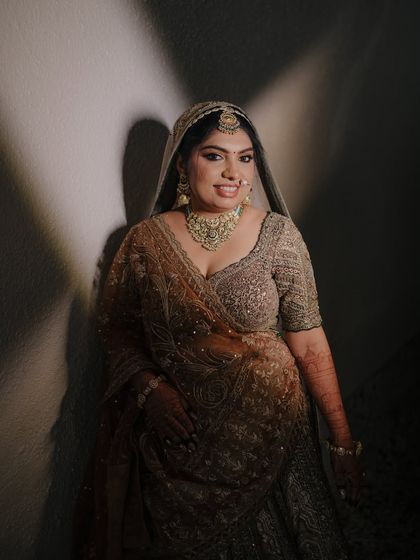 A stunning bridal portrait using dramatic side-lighting. The bride's smile is radiant, and her embroidered lehenga is beautifully showcased.