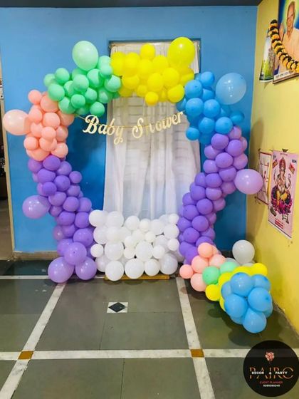 A rainbow-themed baby shower arch. This open-ring design uses blocks of color to create a rainbow effect, with a simple "Baby Shower" sign in the center.
