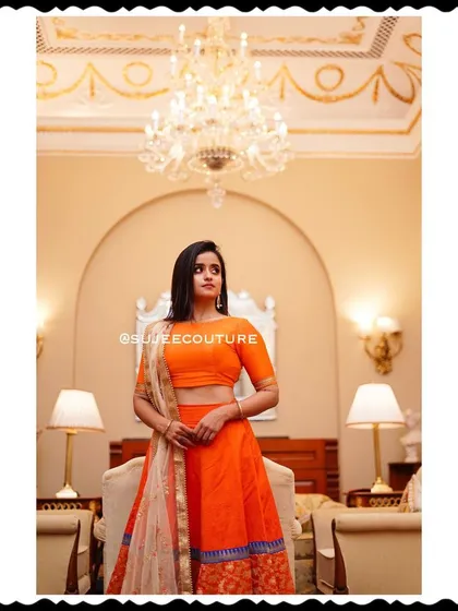 A stunning portrait of Chaitra Vasudevan wearing my custom orange lehenga creation. The outfit's vibrant color and classic design make it a standout piece for any special event.