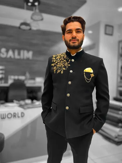 A client wearing a black Jodhpuri jacket with gold floral embroidery on one shoulder. The asymmetrical design is a modern twist on a classic silhouette.