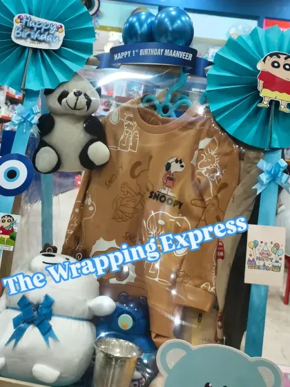 This is a Shinchan themed first birthday hamper for a baby boy named Maanveer. It includes clothes, soft toys, and other goodies in a coordinated blue theme.