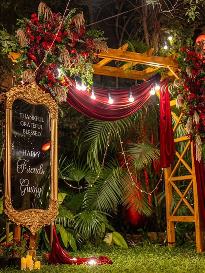A cozy and stylish Friendsgiving dinner in a garden. The decor featured a custom mirror sign, a wooden arch with rich red drapery, and plenty of warm lighting.