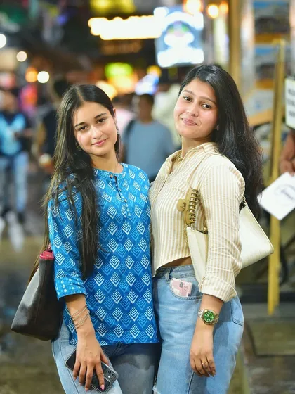 A classic portrait of two friends posing together. The vibrant lights of the night market create a fun and energetic background for their picture.