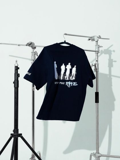 A behind-the-scenes style shot of a black graphic tee on a hanger, surrounded by studio light stands. This gives an authentic, "in the studio" feel.