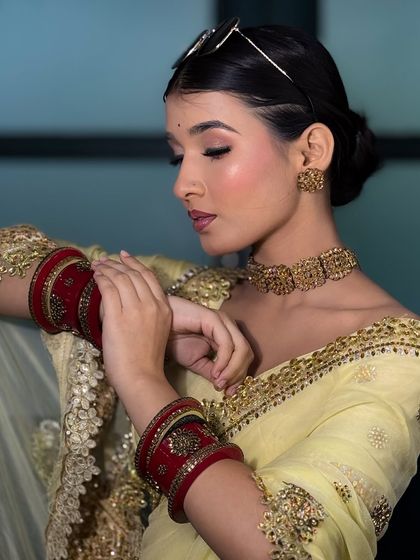 A graceful pose highlighting the bride's red choora against her yellow saree. The makeup is soft and dewy, perfect for a day event.