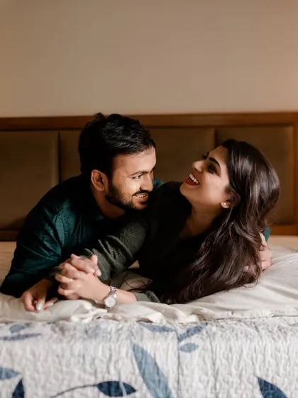 A cozy and intimate indoor shot of the couple laughing together on a bed. This relaxed, lifestyle-type photo captures a private, tender moment.