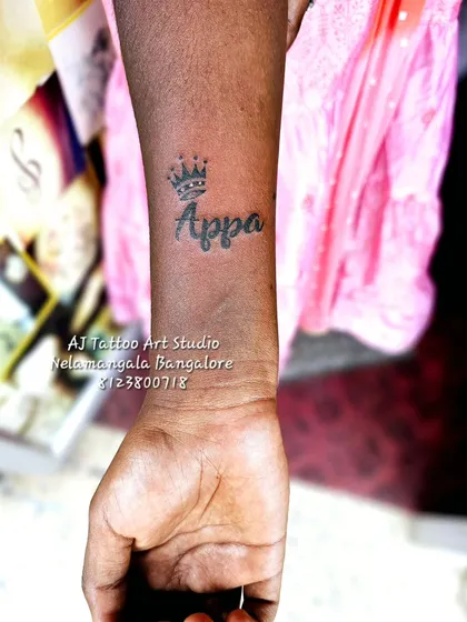 A simple 'Appa' (Dad) tattoo on the wrist with a crown above it.