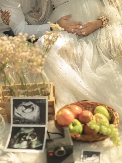 A close-up of a styled picnic, with the sonogram pictures, a vintage camera, and a basket of fruit in the foreground. The focus is on the details that tell the couple's story.