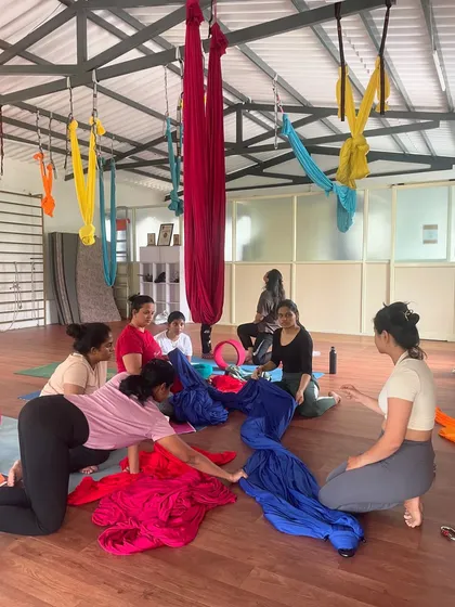 A group of students gathered on the floor, learning the fundamentals of handling the aerial silks. Our training emphasizes hands-on learning from the ground up.