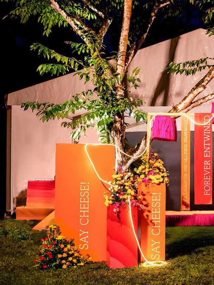 A fun and quirky photo corner with signs that say "Say Cheese!" The area is decorated with colorful blocks, neon light strips, and fringed lampshades hanging from a tree.