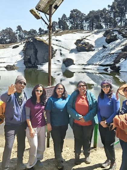 A group of trekkers posing by a serene, snow-edged lake in the Tirthan Valley. It's a perfect mix of easy trekking and beautiful sights.