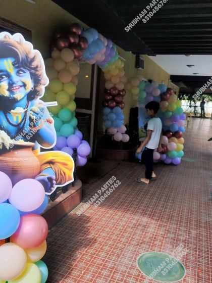 A Krishna themed party entrance with a large character cutout and a pastel balloon arrangement.