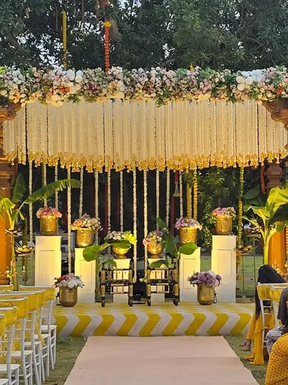 A close-up of our South Indian theme Haldi mandap. The design features carved pillars, brass pots with floral arrangements, and a backdrop of delicate white flower strings, creating an authentic and traditional feel.