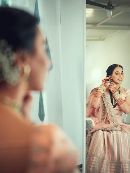 A beautiful getting-ready shot of the bride adjusting her earring in the mirror, with her reflection creating a lovely composition.