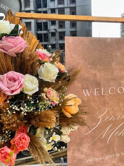 The welcome sign for Zenia's Mehendi, featuring earthy tones and elegant calligraphy, perfectly complemented by a rustic arrangement of pampas grass and roses.