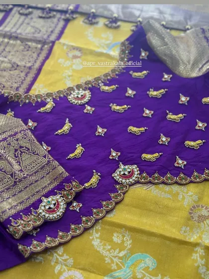 A close-up of our signature jewellery-concept blouse. This royal purple silk blouse is adorned with hand-embroidered mango motifs and kemp stone pendants, creating a look that is both traditional and opulent.