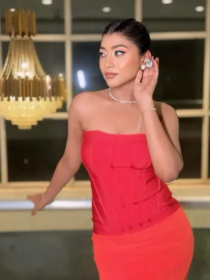 A confident pose in a stunning red dress. The makeup is sharp and defined, with a focus on the eyes and contoured features.
