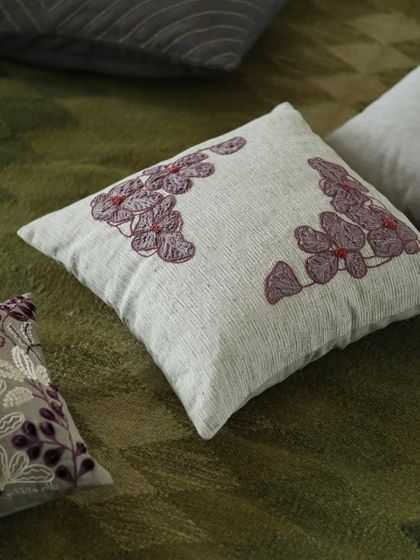 This cushion, also from the 'Ethereal Rose' collection, showcases a more abstract floral embroidery. The design is placed thoughtfully in the corners, allowing the texture of the base fabric to shine through.