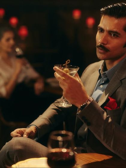 An audience member's perspective, making the viewer feel like they are part of the scene. The sharp suit and martini glass are props that help define his character.