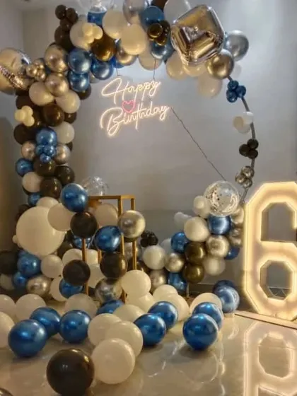 A 6th birthday party with a circular balloon arch in blue, black, and silver, and a '6' marquee light.