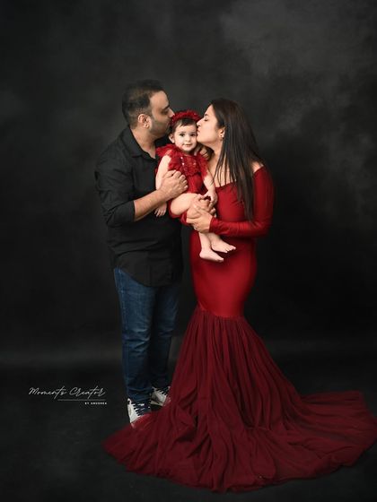 A tender moment between parents and their one-year-old daughter. The classic dark backdrop and elegant red outfits make this a powerful and emotional family portrait.