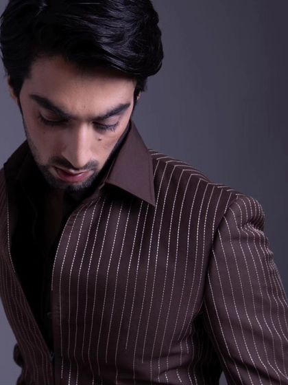 A closer shot of the brown pinstripe jacket, highlighting the subtle texture and the quality of the tailoring in the collar and shoulders.