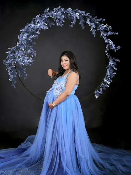A glamorous solo portrait with a blue floral hoop. The mom-to-be's pose is confident and serene, and the long train of her gown creates a stunning visual.