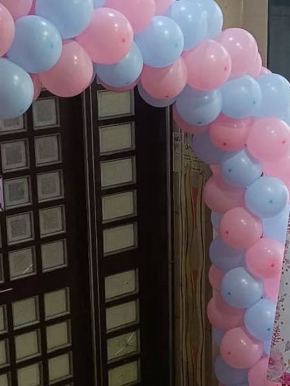 An entrance balloon arch in classic pink and blue for 'Heena's Baby Shower'. The welcome sign next to it continues the gender-neutral color scheme.