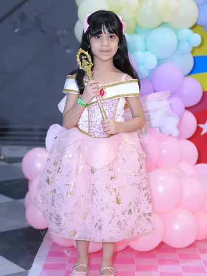 A young guest dressed as a Disney princess holds a magic wand at a pastel-themed party. It's a day for imagination and enchantment.