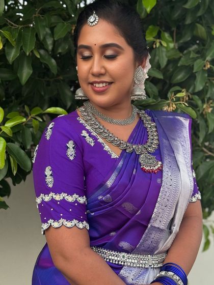 A smiling portrait of Dr. Indhu, showcasing her beautiful silver jhumkas and layered necklaces. This look is perfect for the bride who wants to stand out with a non-traditional choice.