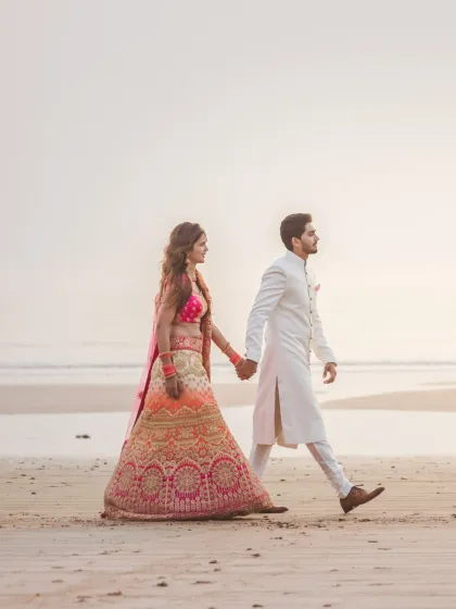A stylish shot of a couple walking hand-in-hand on the beach, capturing their confident stride and elegant wedding attire.