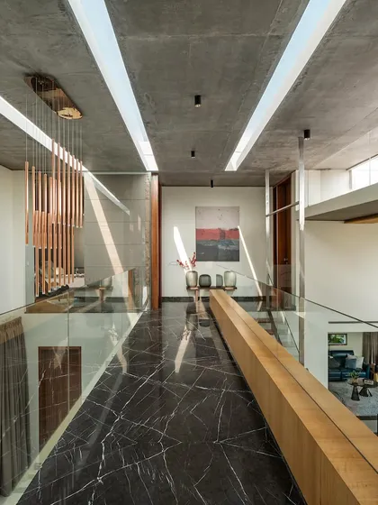 The upper-level corridor features a floor of black marble with dramatic white veining, contrasting with the raw concrete ceiling. Skylights run the length of the space, casting linear patterns of light and shadow.