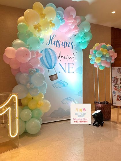 A full view of the 'Onederful' hot air balloon party setup, showing the pastel balloon arch against the custom backdrop, the neon number '1', and the photo collage board on an easel.