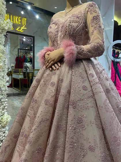 A close-up on the details of our dusty pink ball gown. This shot highlights the illusion neckline, the delicate beadwork on the bodice, and the fun, fluffy feather cuffs on the long sleeves.