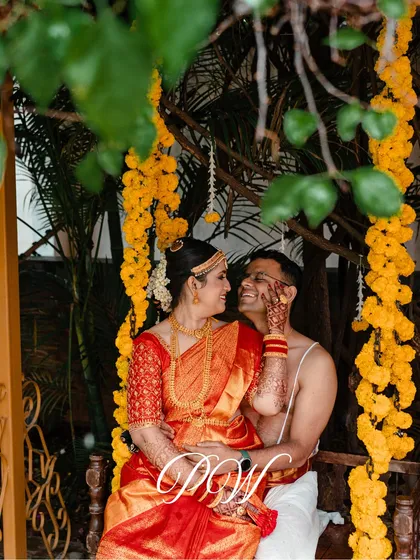 A happy couple sharing a moment on the traditional wedding swing (Oonjal), decorated with bright yellow marigolds. These candid shots are what make a wedding album truly special.